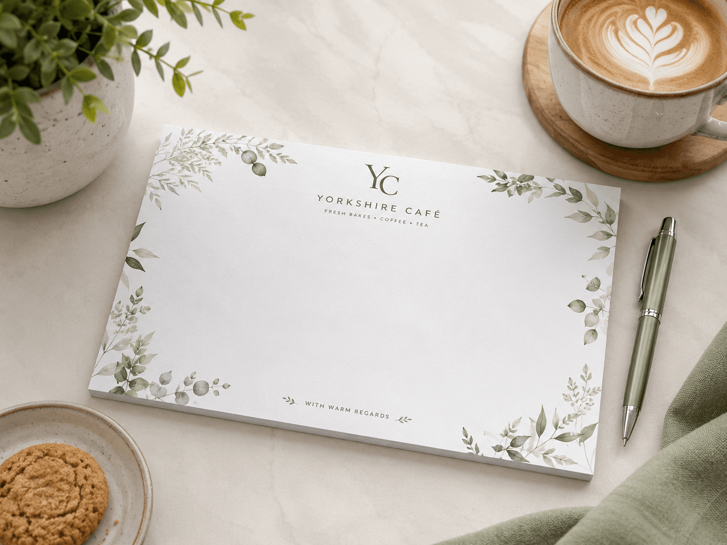 Branded notepad print product laid out beside coffee and stationery